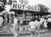 Image of sheet 19850471 photo 3: Auf der Panamericana schleppen Frauen in Plastikbehältern über lange Distanzen Wasser. Ein Mann preist auf der Strasse seine Ware an. Ein Mann schläft auf dem Trottoir. Polizist. Hot Dog stand.in der Innenstadt. Menschengruppe. Wohnung steht zur Vermietung leer. Schlüssel liegen eingebrennt in Kacheln auf dem Gehsteig. Eine junge Frau verkauft ihre Ware auf einem Gehsteig. Sie trägt ein T-Shirt USA. Präsident Napoleon Duarte (gest.) gibt eine PK.
Zentralamerika Centralamerica El Salvador 1985