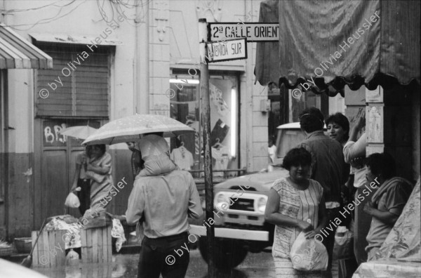 Image of sheet 19850471 photo 35: Auf der Panamericana schleppen Frauen in Plastikbehältern über lange Distanzen Wasser. Ein Mann preist auf der Strasse seine Ware an. Ein Mann schläft auf dem Trottoir. Polizist. Hot Dog stand.in der Innenstadt. Menschengruppe. Wohnung steht zur Vermietung leer. Schlüssel liegen eingebrennt in Kacheln auf dem Gehsteig. Eine junge Frau verkauft ihre Ware auf einem Gehsteig. Sie trägt ein T-Shirt USA. Präsident Napoleon Duarte (gest.) gibt eine PK.
Zentralamerika Centralamerica El Salvador 1985