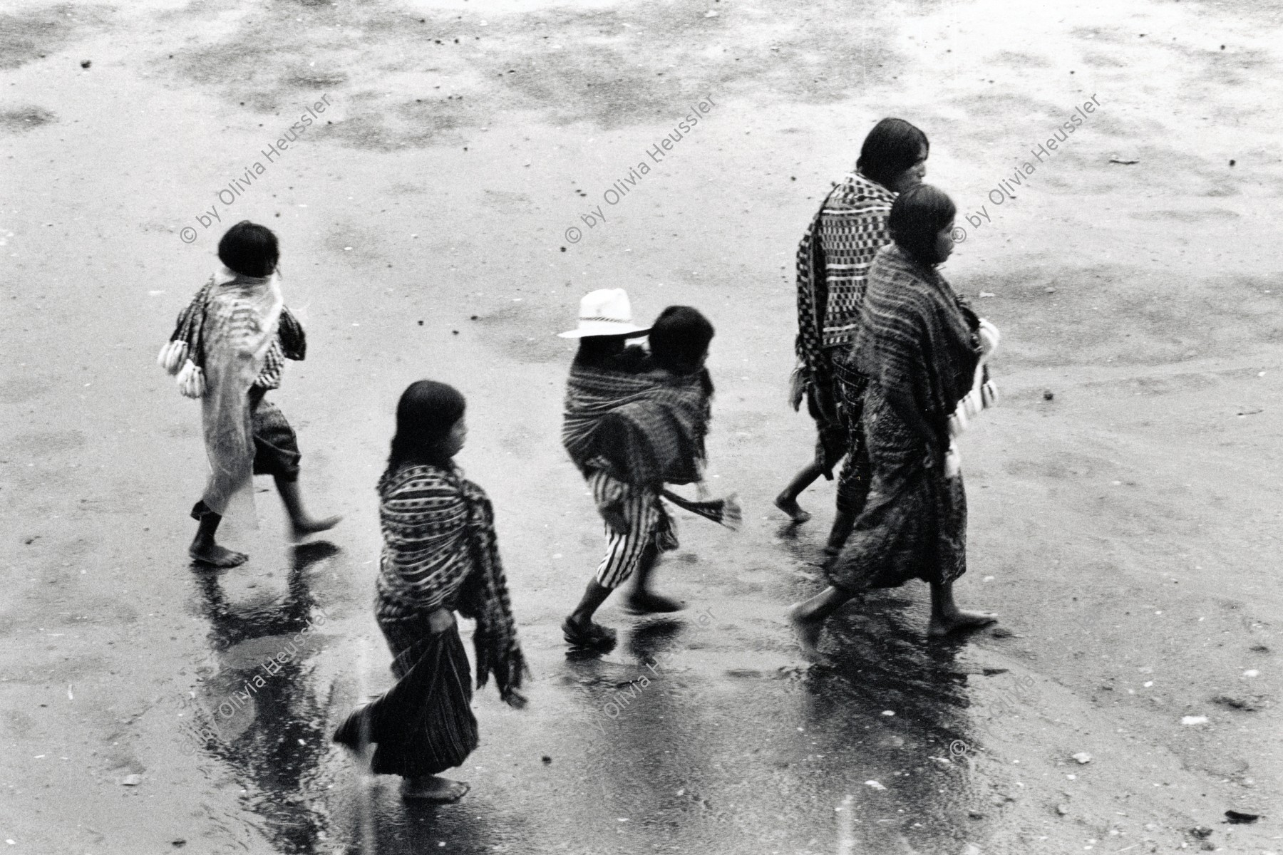 Image of sheet 19850510 photo 24: Auf dem Weg und am Tag der Wahlen . Am Atitlansee. Atitlan Indigena Indianer Indianerinnen. Eine Bauern Familie watet durch den Regen. Die Kinder amüsieren sich in ihren Trachten. Guatemala 1985 √