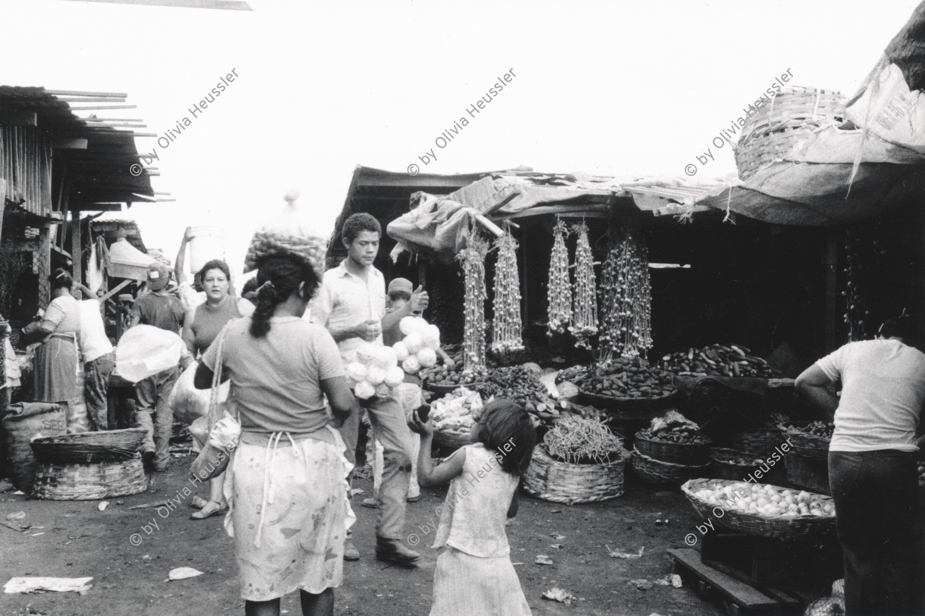 Image of sheet 19870030 photo 26: Strassenszenen in Managua. Versorgung. Marktszenen Mercado Oriental. Frauen verkaufen 
Männer Knoblauch und Kind preisst Ware an. Nicaragua 1987 √