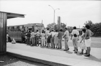 Image of sheet 19870061 photo 17: Bushaltestelle am Mercado R. Huembes. Menschen schleppen und bepacken die Busse. Der Buss fährt nach Masaya. Leute warten auf Buss, ich Olivia heussler spiegle mich im Spiegel des Wartenden. Menschenschlange wartet für den Buss. Managua Nicaragua 1987