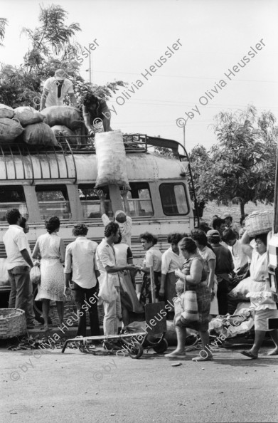 Image of sheet 19870061 photo 5: Bushaltestelle am Mercado R. Huembes. Menschen schleppen und bepacken die Busse. Der Buss fährt nach Masaya. Leute warten auf Buss, ich Olivia heussler spiegle mich im Spiegel des Wartenden. Menschenschlange wartet für den Buss. Managua Nicaragua 1987