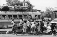 Image of sheet 19870061 photo 6: Bushaltestelle am Mercado R. Huembes. Menschen schleppen und bepacken die Busse. Der Buss fährt nach Masaya. Leute warten auf Buss, ich Olivia heussler spiegle mich im Spiegel des Wartenden. Menschenschlange wartet für den Buss. Managua Nicaragua 1987