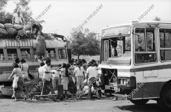 Image of sheet 19870061 photo 7: Bushaltestelle am Mercado R. Huembes. Menschen schleppen und bepacken die Busse. Der Buss fährt nach Masaya. Leute warten auf Buss, ich Olivia heussler spiegle mich im Spiegel des Wartenden. Menschenschlange wartet für den Buss. Managua Nicaragua 1987