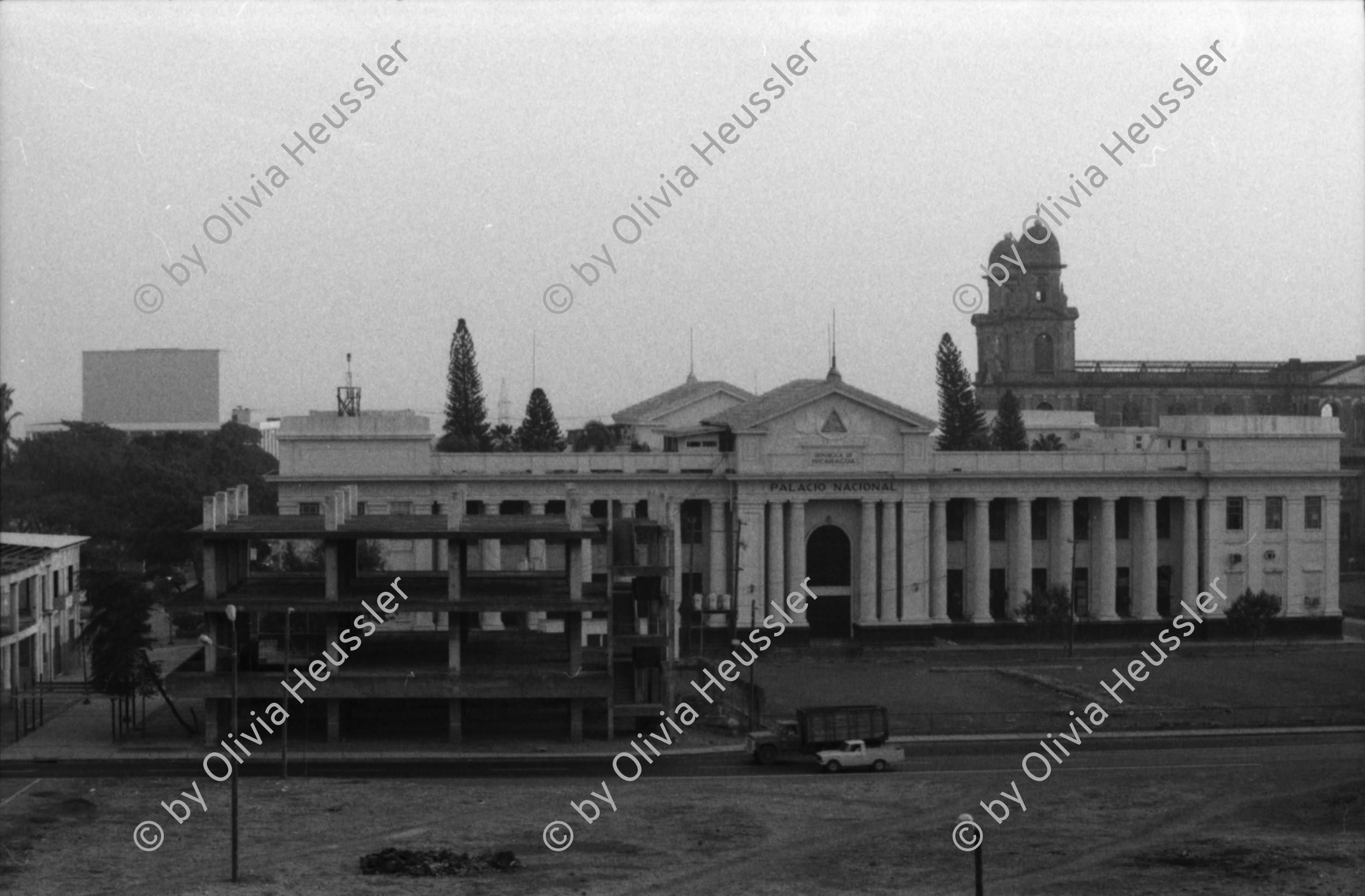 Image of sheet 19870062 photo 32: Gespräch für Schweizer Illustrierte mit Rio Spirgi (gestorben November 2007) 83 jährig und Hanspeter Bürgin. Er ist Chirurg und arbeitet seit 1983 für das Gesundheitsministerium Ministerio de Salud und Centrale Sanitaire Suisse. CSS Heute Medico International Seine Freundin heisst Vogel ist aus Basel.
Palacio National, Correo, (PTT) Postbüro und Kino Cinema Cabrera. Banco de America. Bankgebäude Altstadt von Managua. FSLN Frente Sandinista de Libéracion Nacional Lettern am Haus Wandmalerei. Graffitti Hotel Intercontinental im Hintergrund Managua Nicaragua 1987