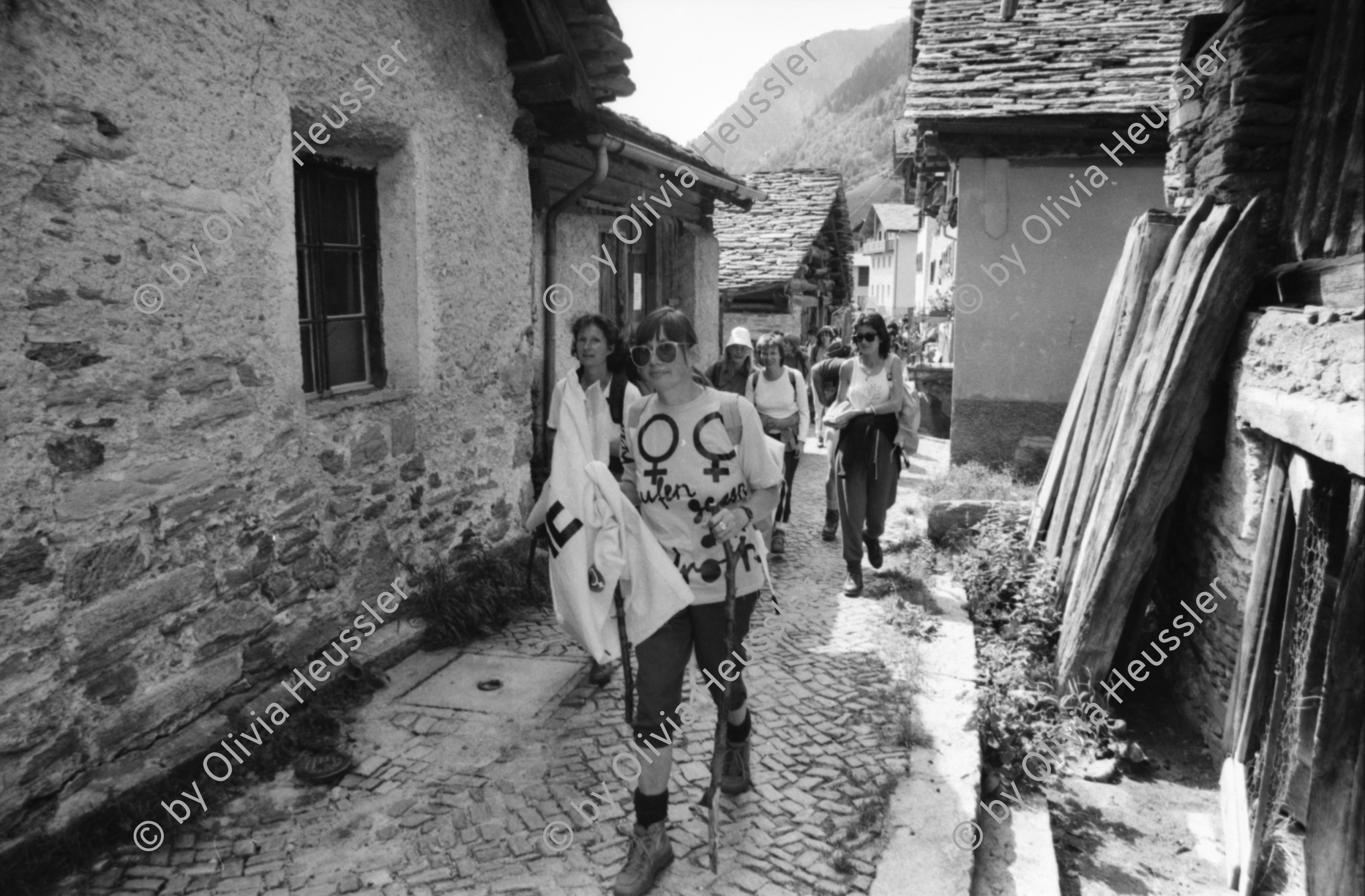 Image of sheet 19870251 photo 35: Frauen Protest Wanderung gegen den Plan eines Pumpspeicherkraftwerks im Val Madris Passüberquerung auf alter Rinder Treppe Kuhtreppe für Kühe ins Bergell. Graubünden Einmarsch ins Dorf Soglio.  Rentner Zuschauer sitzen im Dorf. Transparent «Wir Frauen haben genug Energie»
Bergell Soglio Graubünden Schweiz 1987