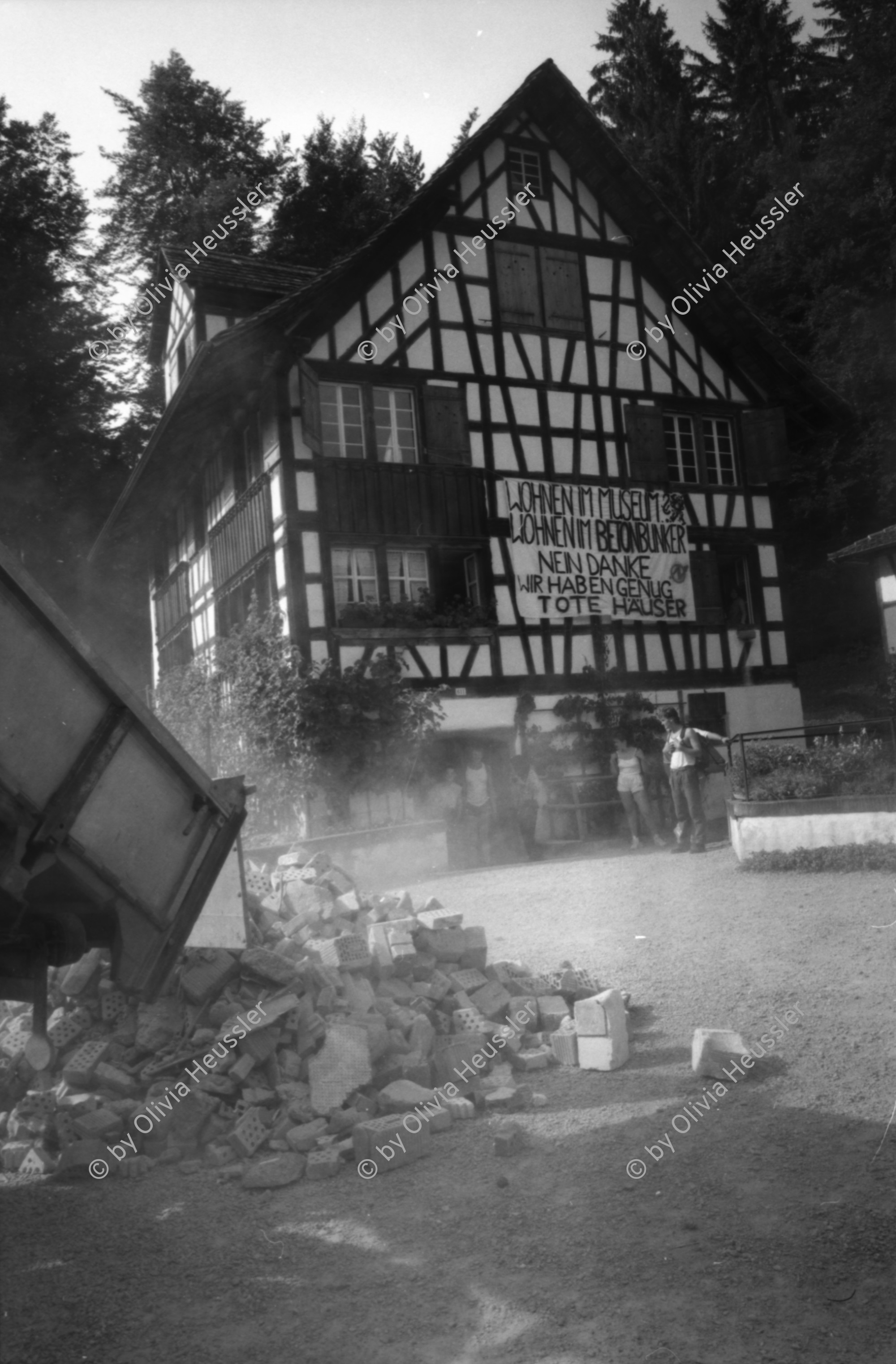 Image of sheet 19870271 photo 28: frtsg. 870270 Besetzung Ballenberg freiluft Museum Diakonissin besucht Besetzer Innen Besucher Innen. Bürgermeister Anderfuhren auf Besuch Lastwagen mit Schutt aus Zürich wird  vor Zürcher Bauernhaus entleert. 'Nieder mit billigem Wohnraum, die Stadt Zürich präsentiert die saubere Lösung. zum Beispiel: HÖSCHGASSE. Kanton Bern
Kind in Brunnen Erwachsene darumherum. Zürich