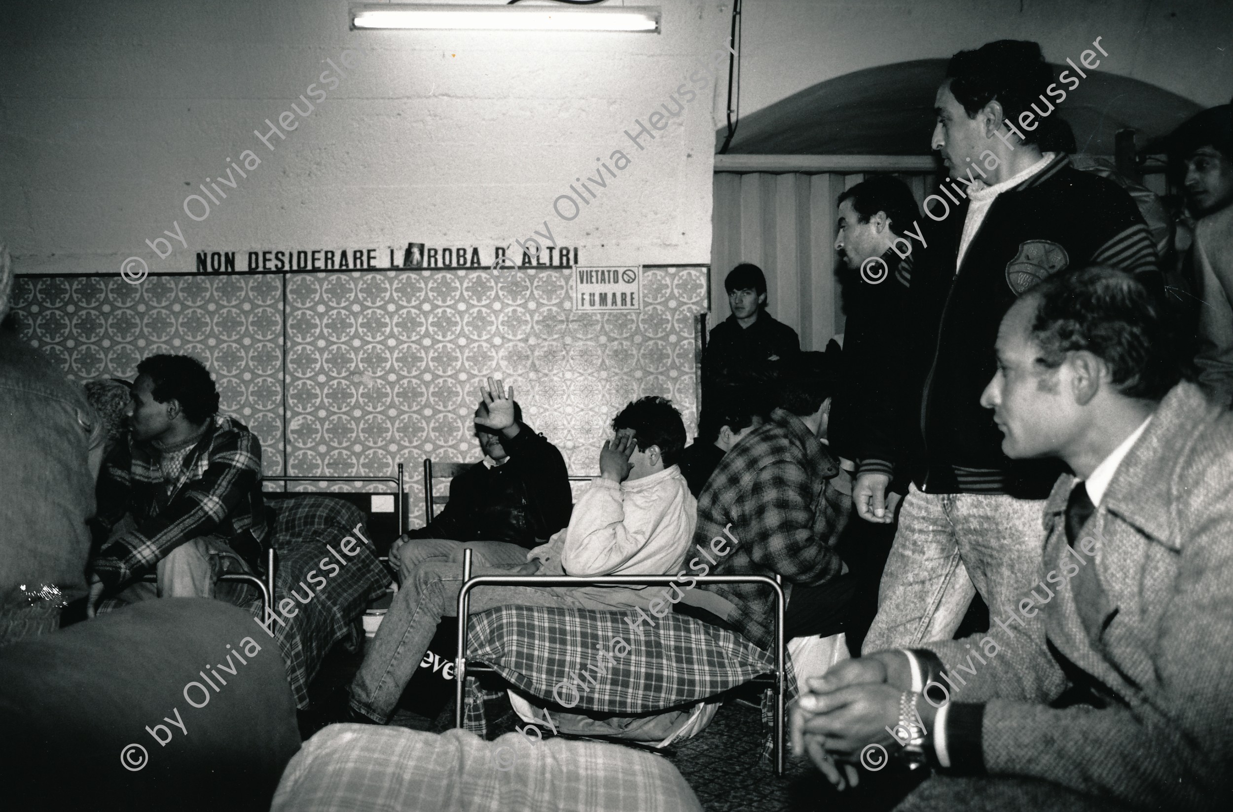 Image of sheet 19870390 photo 5: Im Auffanglager für die von der Schweiz abgewiesenen Flüchtlinge und Obdachlose unter den Geleisen des Zentral Bahnhofs, Mailand 1987. 

Bei Fratello Ettore der Raum dient auch als Kirche, Schlaf- und Essraum. Bevor die vorwiegend aus Nordafrika kommenden islamischen Männer ihre Suppe kriegen, müssen sie sich die christliche Messe anhören.Viele verdecken ihre Gesichter vor der Camera und mir. Betten stehen da. Mailand Italien Italy Refugees Asyl Asylanten Exhibition