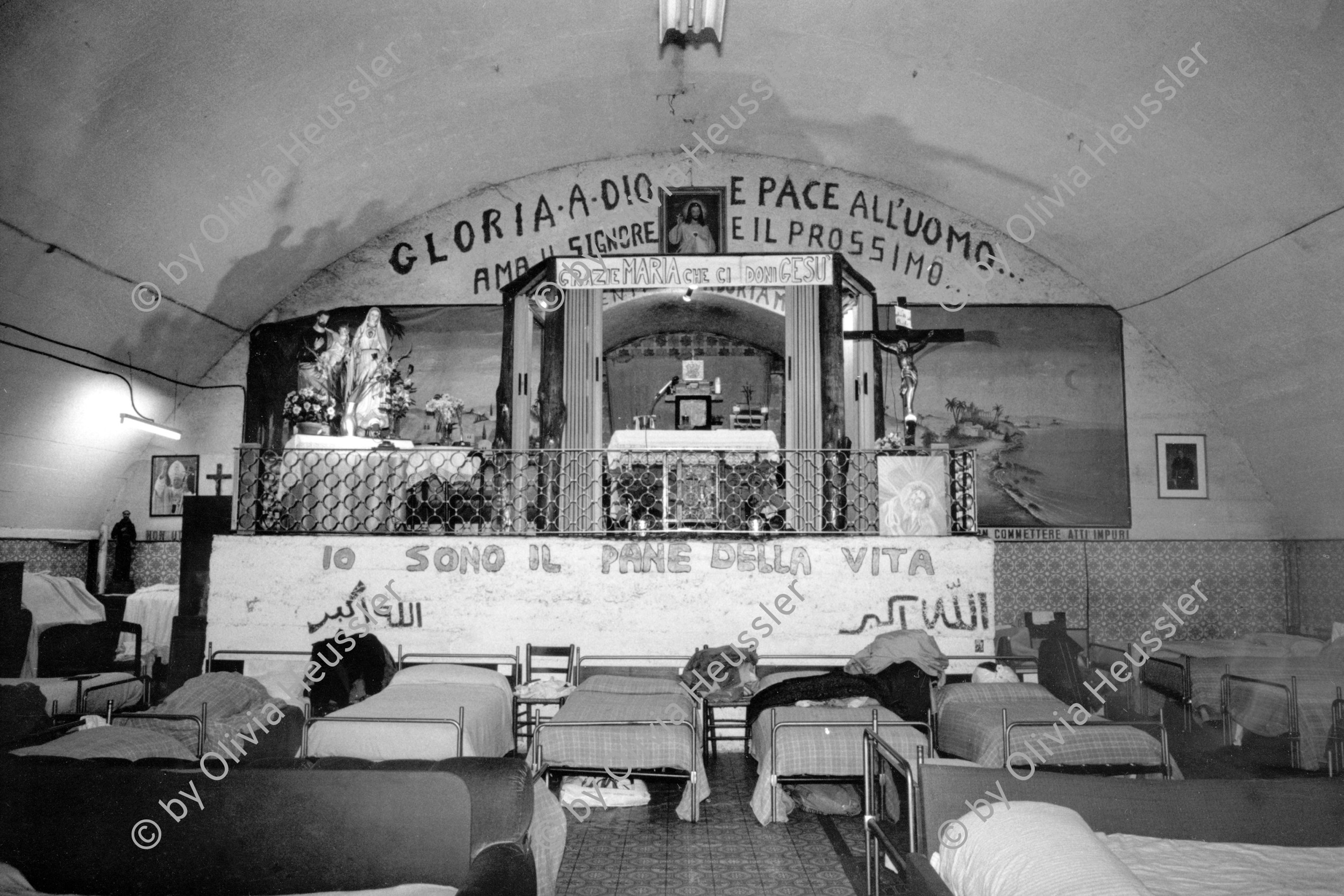 Image of sheet 19870390 photo 27: Delegation von Kaplan Koch. Besuch im Auffanglager für von der Schweiz abgewiesene Flüchtlinge und Obdachlose unter den Geleisen des Zentral Bahnhofs in Mailand. Bei Fratello Ettore der Raum dient auch als Kirche, Schlaf- und Essraum für Männer. Betten stehen da. Vor einem Bild eines Heiligen der auch liegt, nur nicht so bequem. Milano Italy Asylum seekers √
© 1987, OLIVIA HEUSSLER / www.clic.li