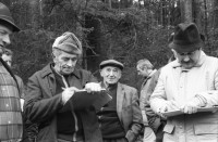 Image of sheet 19880040 photo 1: alter Männer stehen zusammen an Holzgant.Sie schreiben sich die Preise auf. Percy Heussler ist auch dabei. Nr. 12 und 13. Die langen Holz Stiehle zum Cervelats Braten liegen bereit. Die Männer braten Cervelats über dem Feuer. Ein alter Mann zeigt in die Luft. Die Cervelats liegen zum Braten bereit. Die Männer geniessen etwas warmes in der winterlichen Kälte. (!) Holzgant Holzverarbeitung Fällanden Kanton Zürich Schweiz wood forest market man men meat sausage