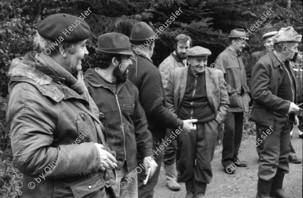 Image of sheet 19880040 photo 11: alter Männer stehen zusammen an Holzgant.Sie schreiben sich die Preise auf. Percy Heussler ist auch dabei. Nr. 12 und 13. Die langen Holz Stiehle zum Cervelats Braten liegen bereit. Die Männer braten Cervelats über dem Feuer. Ein alter Mann zeigt in die Luft. Die Cervelats liegen zum Braten bereit. Die Männer geniessen etwas warmes in der winterlichen Kälte. (!) Holzgant Holzverarbeitung Fällanden Kanton Zürich Schweiz wood forest market man men meat sausage