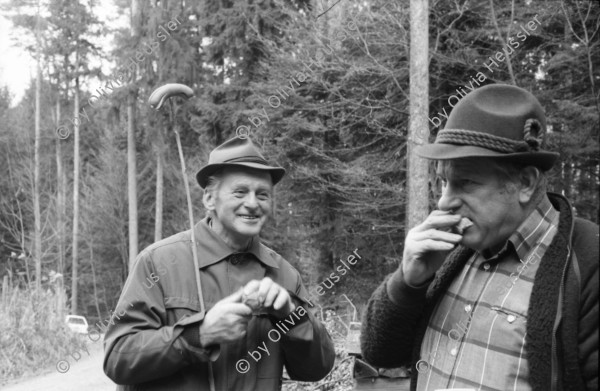 Image of sheet 19880040 photo 33: alter Männer stehen zusammen an Holzgant.Sie schreiben sich die Preise auf. Percy Heussler ist auch dabei. Nr. 12 und 13. Die langen Holz Stiehle zum Cervelats Braten liegen bereit. Die Männer braten Cervelats über dem Feuer. Ein alter Mann zeigt in die Luft. Die Cervelats liegen zum Braten bereit. Die Männer geniessen etwas warmes in der winterlichen Kälte. (!) Holzgant Holzverarbeitung Fällanden Kanton Zürich Schweiz wood forest market man men meat sausage