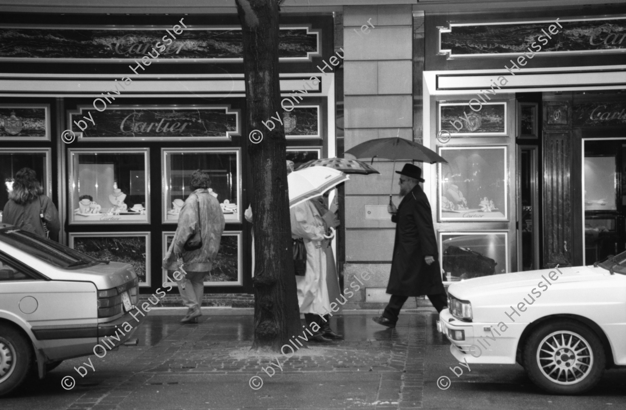 Image of sheet 19880250 photo 17: Szene an der Bahnhofstrasse. Frauen in Pelzmäntel unter Regenschirmen mit Hunden vor Schaufenster. In Strassenbahn einsteigend. Vor bemalter Strassenbahn. Fancy dreinschauend. 
Granitskulptur (1983) von Max Bill
Der Schweizer Künstler Max Bill schuf 1983 die begehbare «Pavillon-Skulptur» – ein Beispiel für klare Linien –, die heute an erstklassiger Lage vor dem Zürcher Hauptsitz der Grossbank UBS an der Bahnhofstrasse steht. Die streng konzipierte, von Logik und Klarheit geprägte Konstruktion aus hochpolierten, grauen Granitelementen war anfänglich äusserst umstritten.
Paare leicht gestresst wirkend. Männer Gruppe. Plakat für Annabelle wird 50.
Zürich 1988