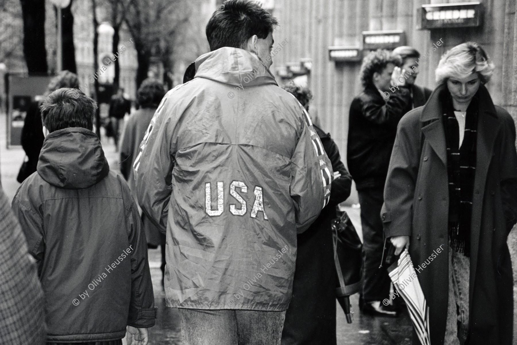 Image of sheet 19880270 photo 13: Mann mit 'USA Beschriftung auf dem Rücken seiner Windjacke. Zürcher Bahnhofstrasse. Zürich Kreis 1 eins Down town Old town Winter 1988 √ Passanten Schweiz Switzerland swiss shoping hand kid child woman Europe