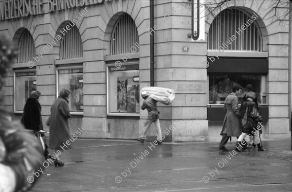 Image of sheet 19880270 photo 20: frstg. 880260        Damen plaisieren vor Schaufenster Damen unter Regenschirmen. Mann mit USA auf dem Rücken. Herren mit Hundchen. gefolgt von einem Hund. in Pelzmäntel an der Zürcher Bahnhofstrasse. Zürich 1988