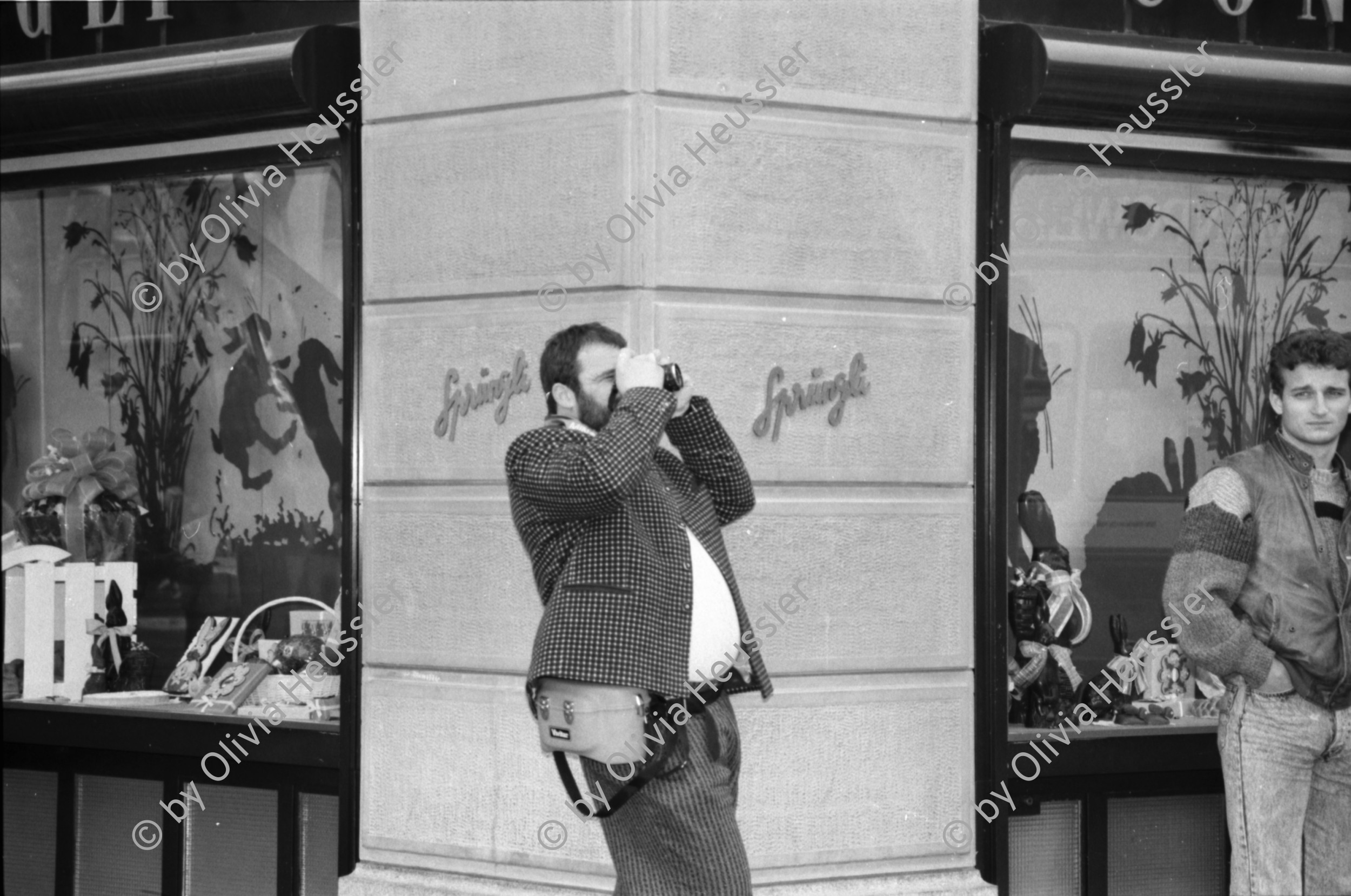 Image of sheet 19880300 photo 10: frtsg. 880290 Pelzmäntel. Geschäftsmann ruht sich aus. Dame in Bewegung. Damen mit Hund. Bei Sprüngli fotografiert ein Tourist mit dickem Bauch Damen vor Reisebüro SBB- Strassenbahn Tram Dame kokettiert. Bewegungen mit Auto. Verkehrs Polizei gibt Busse. Vor Gübelin. Im Regen rennen die Leute über den Paradeplatz. Die Strassenbahn hält. Bahnhofstrasse Zürich 1988