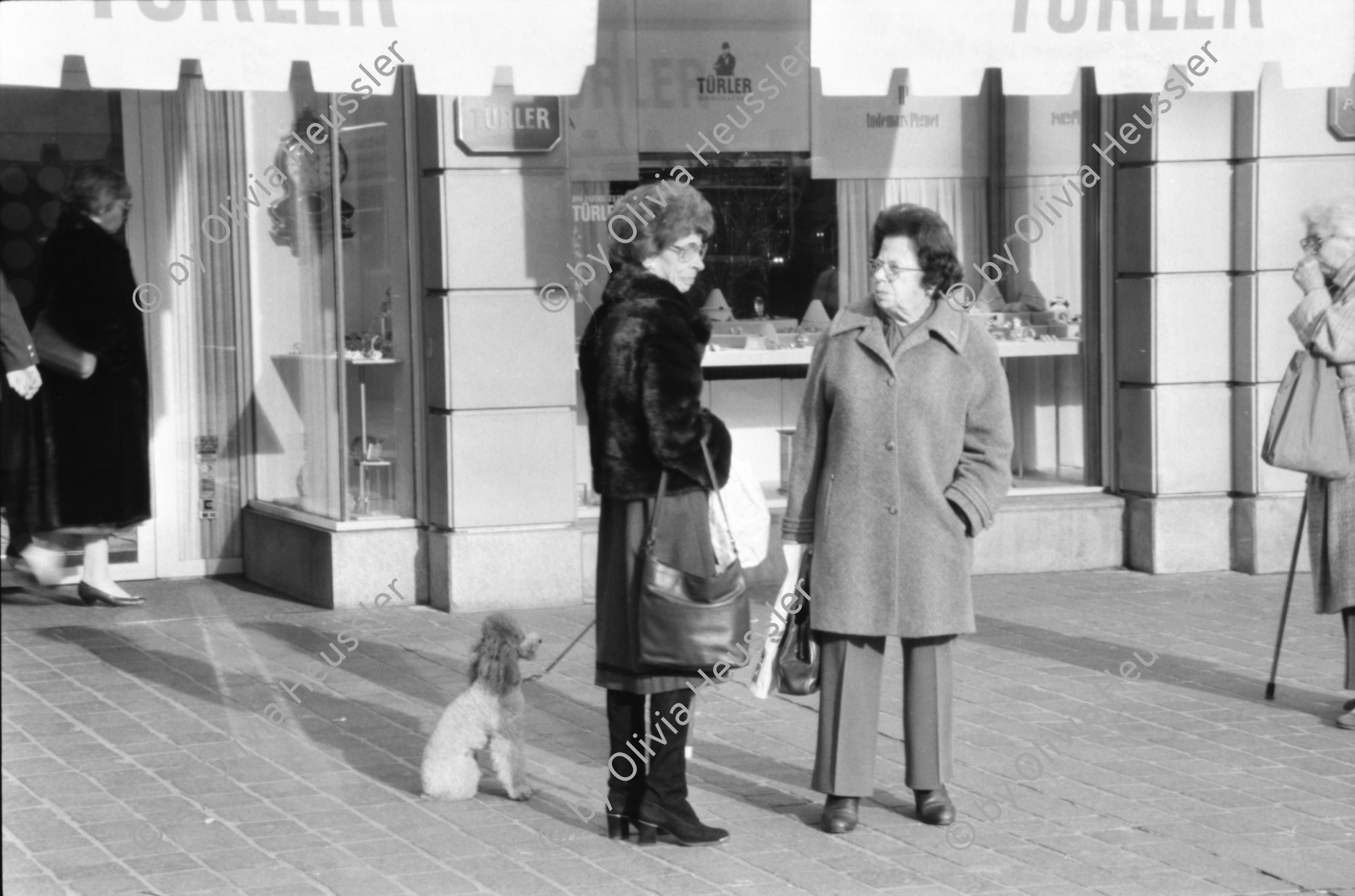 Image of sheet 19880300 photo 8: frtsg. 880290 Pelzmäntel. Geschäftsmann ruht sich aus. Dame in Bewegung. Damen mit Hund. Bei Sprüngli fotografiert ein Tourist mit dickem Bauch Damen vor Reisebüro SBB- Strassenbahn Tram Dame kokettiert. Bewegungen mit Auto. Verkehrs Polizei gibt Busse. Vor Gübelin. Im Regen rennen die Leute über den Paradeplatz. Die Strassenbahn hält. Bahnhofstrasse Zürich 1988