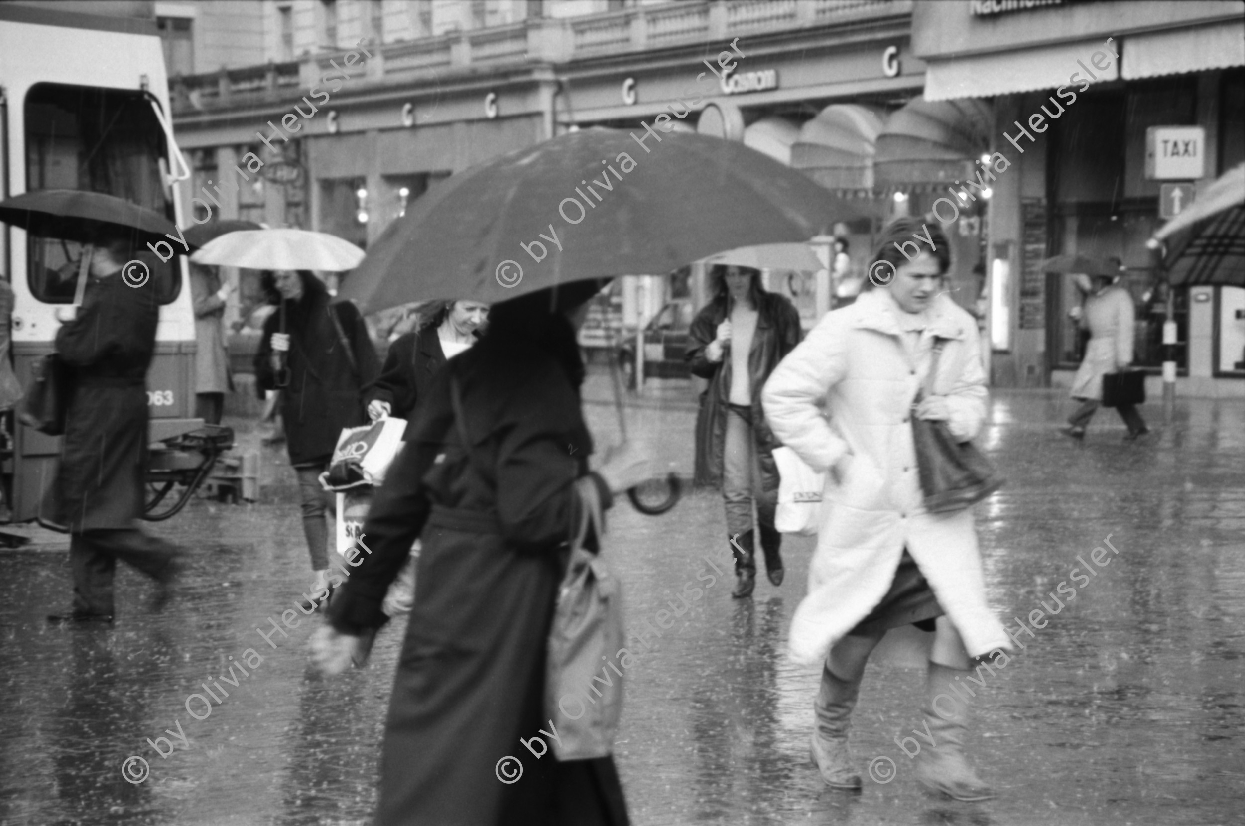 Image of sheet 19880310 photo 20: frtsg. 880300 Bewegung auf dem Paradeplatz an der Zürcher Bahnhofstrasse, es regnet die Menschen rennen gestresst durch den Regen. Unter dem Regenschirm einstellen von täglichem Schadstoffpegel. Unter Regenschirmen Bewegung. Mit Strassenbahn PassantInnen. Zwei Knaben in Strassenbahn. Tram Zürich 1988