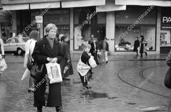 Image of sheet 19880310 photo 29: frtsg. 880300 Bewegung auf dem Paradeplatz an der Zürcher Bahnhofstrasse, es regnet die Menschen rennen gestresst durch den Regen. Unter dem Regenschirm einstellen von täglichem Schadstoffpegel. Unter Regenschirmen Bewegung. Mit Strassenbahn PassantInnen. Zwei Knaben in Strassenbahn. Tram Zürich 1988