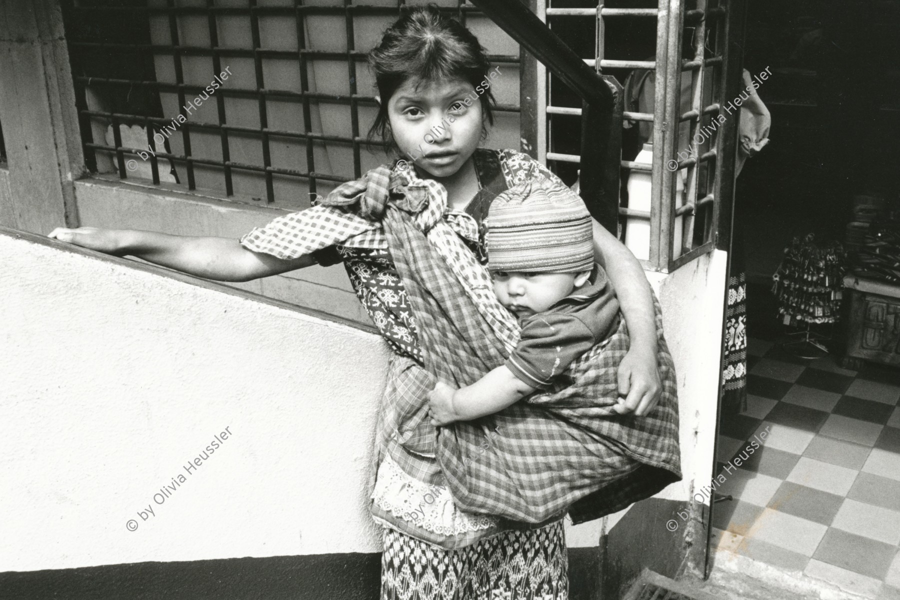 Image of sheet 19881020 photo 15: Eine Indigena mit Kleinkind im Tragtuch, Guatemala City,1988. 
 
girl with baby in bag baby sling wrap