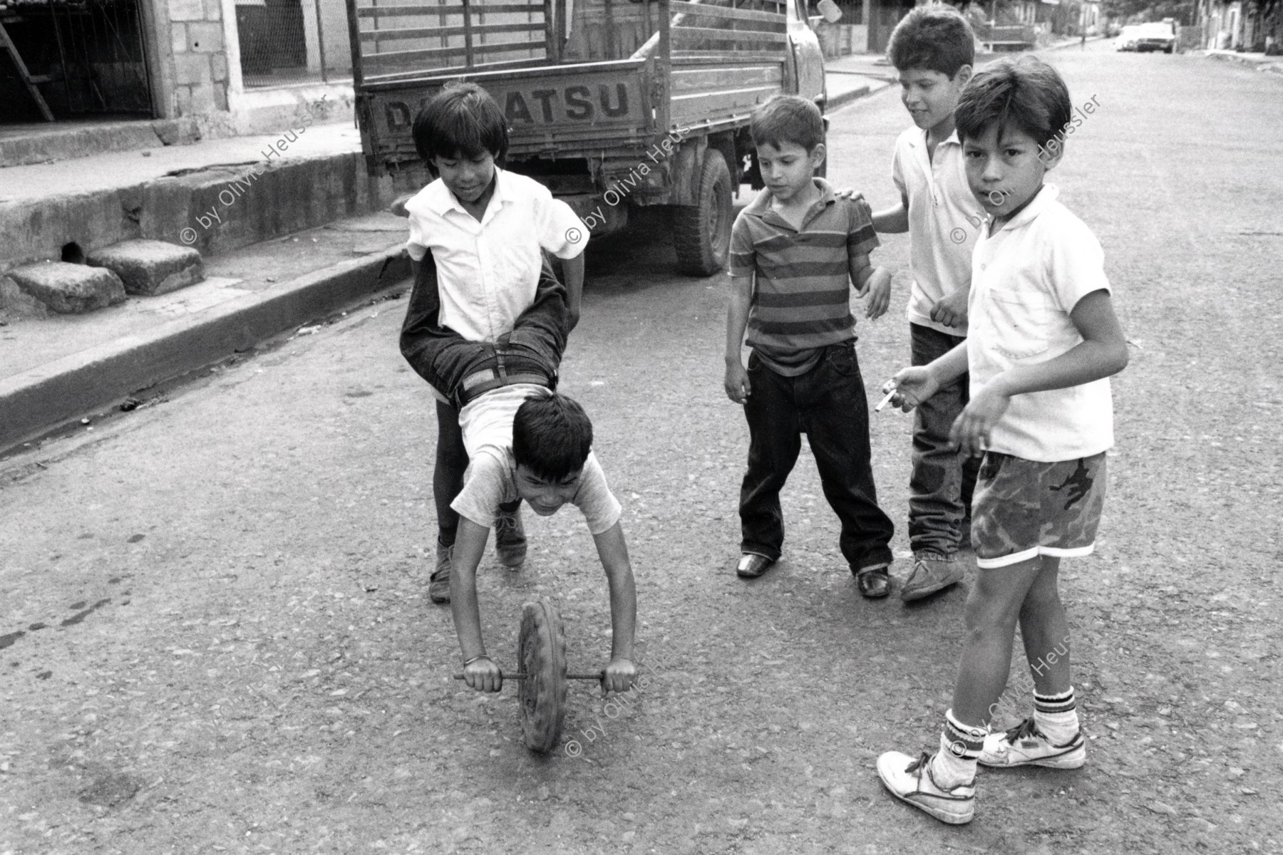 Image of sheet 19881110 photo 14: Eine Gruppe von Kindern spielt mit einem Holzrad auf der Strasse, Managua Nicaragua 1988.