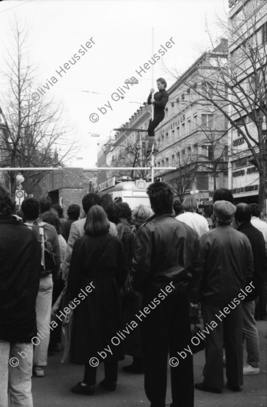 Image of sheet 19890120 photo 1: Irene Schweizer am Piano Portrait gibt unter der Pavillon Skulptur* von Max Bill an der Bahnhofstrasse ein Konzert während ein Seiltänzer eine Performance gibt. Bankenpiquett gegen die CH-er Finanzpolitik in Südafrika. Protest. Bankangestellte essen Lunch gehend auf der Bahnhofstrassse.
*Granitskulptur (1983) von Max Bill
Der Schweizer Künstler Max Bill schuf 1983 die begehbare «Pavillon-Skulptur» – ein Beispiel für klare Linien –, die heute an erstklassiger Lage vor dem Zürcher Hauptsitz der Grossbank UBS an der Bahnhofstrasse steht. Die streng konzipierte, von Logik und Klarheit geprägte Konstruktion aus hochpolierten, grauen Granitelementen war anfänglich äusserst umstritten. Zürich 1989 Bahnhofstrasse