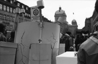 Image of sheet 19890370 photo 7: Frau steht eingepackt in der Sonne. Welteinheit durch Weltordnung' steht da auf einer Tafel einer religiösen Sekte. Ein Karton AKW wird an der Demonstration gegen Atomkraftwerke herumgetragen. Transparent: 'Für die sofortige Stilllegung der herrschenden Klasse' Portrait von Viktor Braun. Giovanni Schuhmacher mit Fahne und dem Anarchisten A vor Bundeshaus in Bern. Eine Frau muss über die Abschrankung der Polizei auf den Bundeshausplatz steigen . Meine Bilder im Hotel Bern. Nicaragua von sieben Schweizer Photographen und Photographinnen. Reithalle Interieur Skateborder Bern 1989