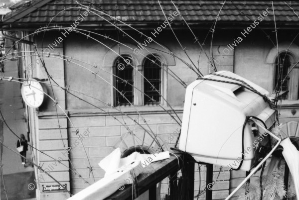 Image of sheet 19890500 photo 8: Ankerstrasse. Besetzt. Eingezäunt mit Stacheldraht versuchen die Bewohner Innen sich gegen eine Räumung zu wehren. Nur symbolisch. Auch der Hühnerhof auf dem Dach ist in Gefahr. Von dort sieht frau auf die Kanonengasse runter. Vis a Vis die Kasernen Uhr. Transparent Räumungsstop. Gänse Kopf hängt über Balkon Geländer. Computer steht auf Balkon Geländer. Zürich 1989 Wohnungsnot Hausbesetzung