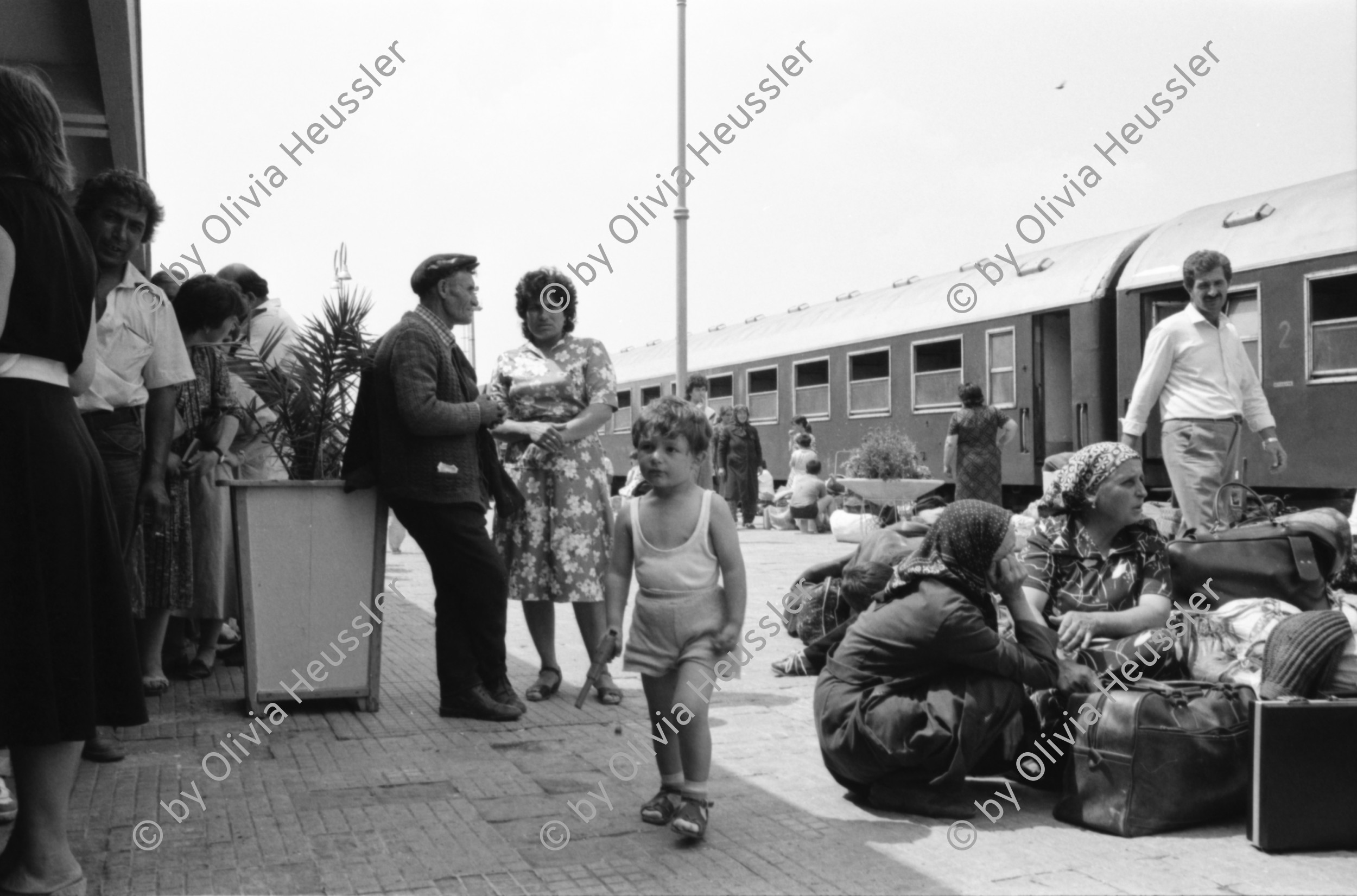Image of sheet 19890600 photo 15: 34. Tag des Exodus türkischstämmiger 'Ausflügler', wie sie in Bulgarien genannt werden. Deportierte in der Türkei. Lastwagenschlage an der Türkisch-Bulgarischen Grenze. Auf dem Bahn-Quai von Kapikule sitzen und liegen hunderte von Türkischstämmigen BulgarInnen mit ihren Familien erschöpft in einem grossen elenden Durcheinander. Die Türkische Fahne bedeutet für viele das Symbol eines 'freien' Landes. In Bulgarien hat man sie gezwungen ihre Namen und ihre Sprache zu ändern. Oezal benützt die ca 300'000 Bulgaren für seine Wahlkampagne. Viele Kinder weinen unaufhörlich vor Erschöpfung. In Bergen von Hab und Gut entdecke ich ganze Wohnungseinrichtungen. Der Duty Free Laden ist geschlossen. Die Güterwagen, in denen die Menschen tagelang eingesperrt reisen mussten, werden nach ihrer Leerung wieder zurückfahren und noch mehr Familien in ihr Unglück stürzen. Türkei Turkey Bulgarian Refugees 1989