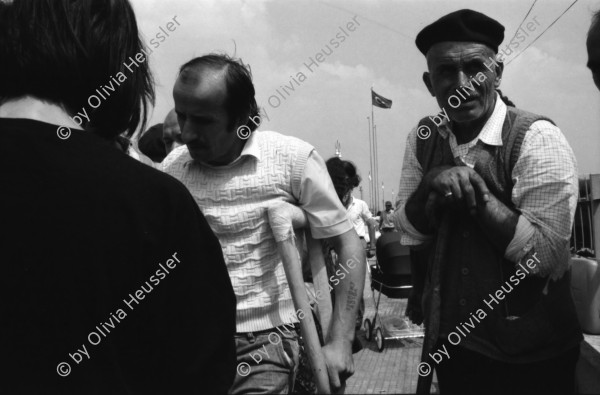 Image of sheet 19890620 photo 1: Auf dem Bahnsteig von Kapikule entdecke ich immer wieder zwischen Sack und Pack vereinsamte Menschen im Elend. Hab und Gut. Einwanderungsbüro. Türkische Fahne. Eine Hand zeigt auf den leeren Güterwagen, wo nicht nur Hausrat transportiert wird, sondern Menschen über 10 Stunden ohne Frischluft und Wasser reisen. Türkei Kapikule 1989