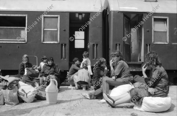 Image of sheet 19890620 photo 36: Auf dem Bahnsteig von Kapikule entdecke ich immer wieder zwischen Sack und Pack vereinsamte Menschen im Elend. Hab und Gut. Einwanderungsbüro. Türkische Fahne. Eine Hand zeigt auf den leeren Güterwagen, wo nicht nur Hausrat transportiert wird, sondern Menschen über 10 Stunden ohne Frischluft und Wasser reisen. Türkei Kapikule 1989