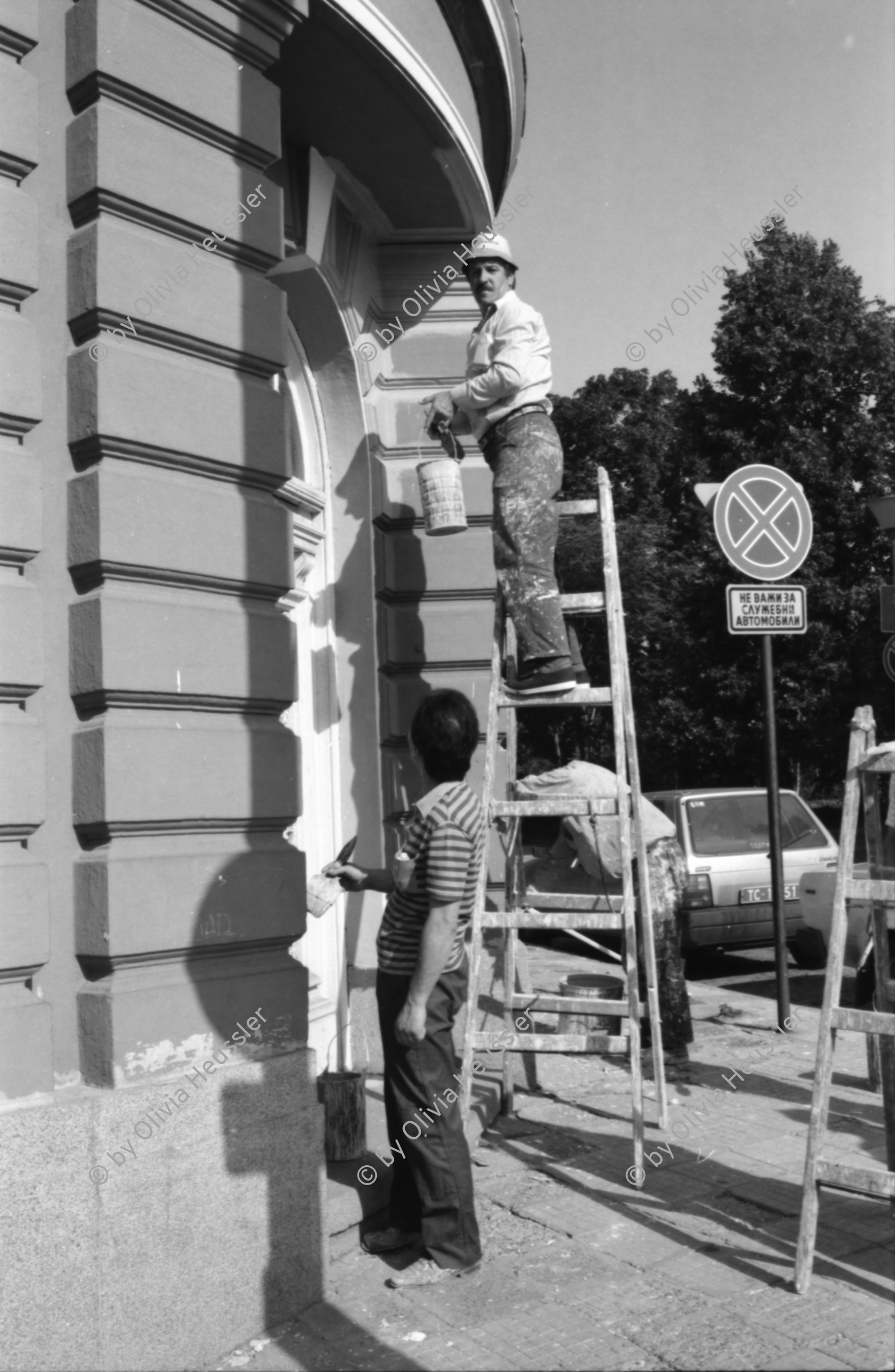 Image of sheet 19890650 photo 14: Eine Bauern-Familie posiert für mich auf dem Gehsteig, nachdem
 sie mich mit Gemüse beschenkt haben. Auf dem Rückweg nach Sofia.
 Ein Orthodoxer auf dem Kirchenplatz in Sofia. Die Moschee in
 Sofia. Ein Mann spritzt die Pflanzen. Zwei alte Männer betrachten
 die Preise für den Kohl. Maler bei der Arbeit. Mercedes Benz.
 Vater und Sohn auf einer Parkbank. Maja Wicki und Djanko und
 Olivia und Maja auf dem Vitussi. Mädchen benützt Grossmutter als
 Gummitwist Halterin. Im Hotel (Nr. 22)steht Maja nach einem
 schlechten Traum wie ein Gespenst da. Bus Nr. 83 Endstation. Die
 Frauen und Männer gehen zur Arbeit in die Fabriken am Stadtrand
 von Sofia. Ziege spaziert. Die zwei Roma bei ihrer Arbeit als Kesselflicker in Razgrad. Bulgaria Bulgarien 1989