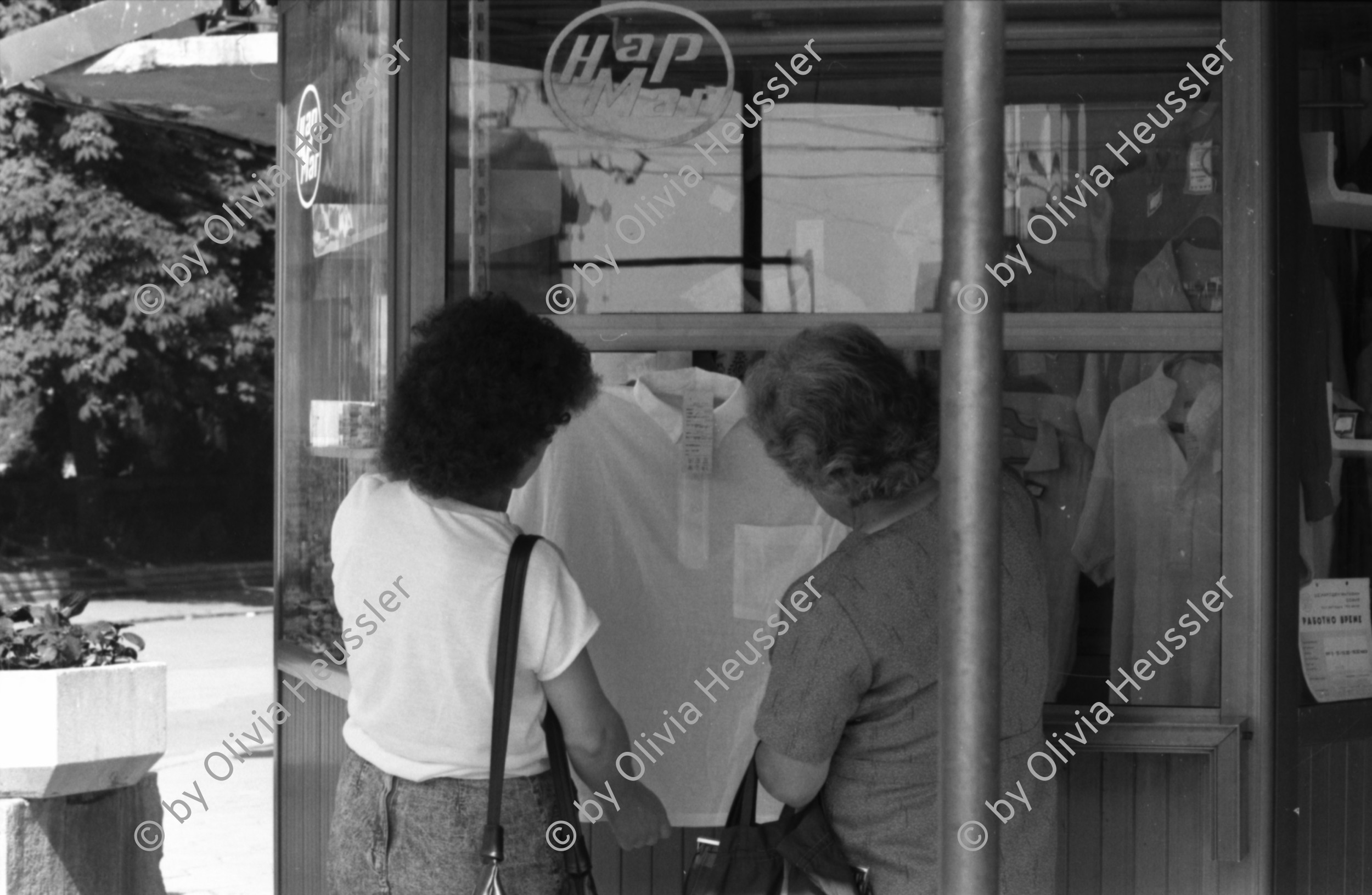 Image of sheet 19890651 photo 5: Ein türkischstämmiges Ehepaar piknikt in einem Restaurant! zwei Frauen betrachten eine Bluse. Mann schläft in Lada. Maja Wicki überquert Strasse. Szenen in der Altstadt und Einkaufsstrasse. Altes Bauernehepaar verkauf Gemüse. Schatten von Maja. Alter Mann mit Matrosenmütze. Mutter mit Kleinkind am Busen. Kindergruppe macht Ausflug und kämpft sich über Pfütze. Mahlzeit! In Volksküche. Unfertige Fussgängerpassage. Hauptplatz. Sofia Bulgaria Bulgarien 1989