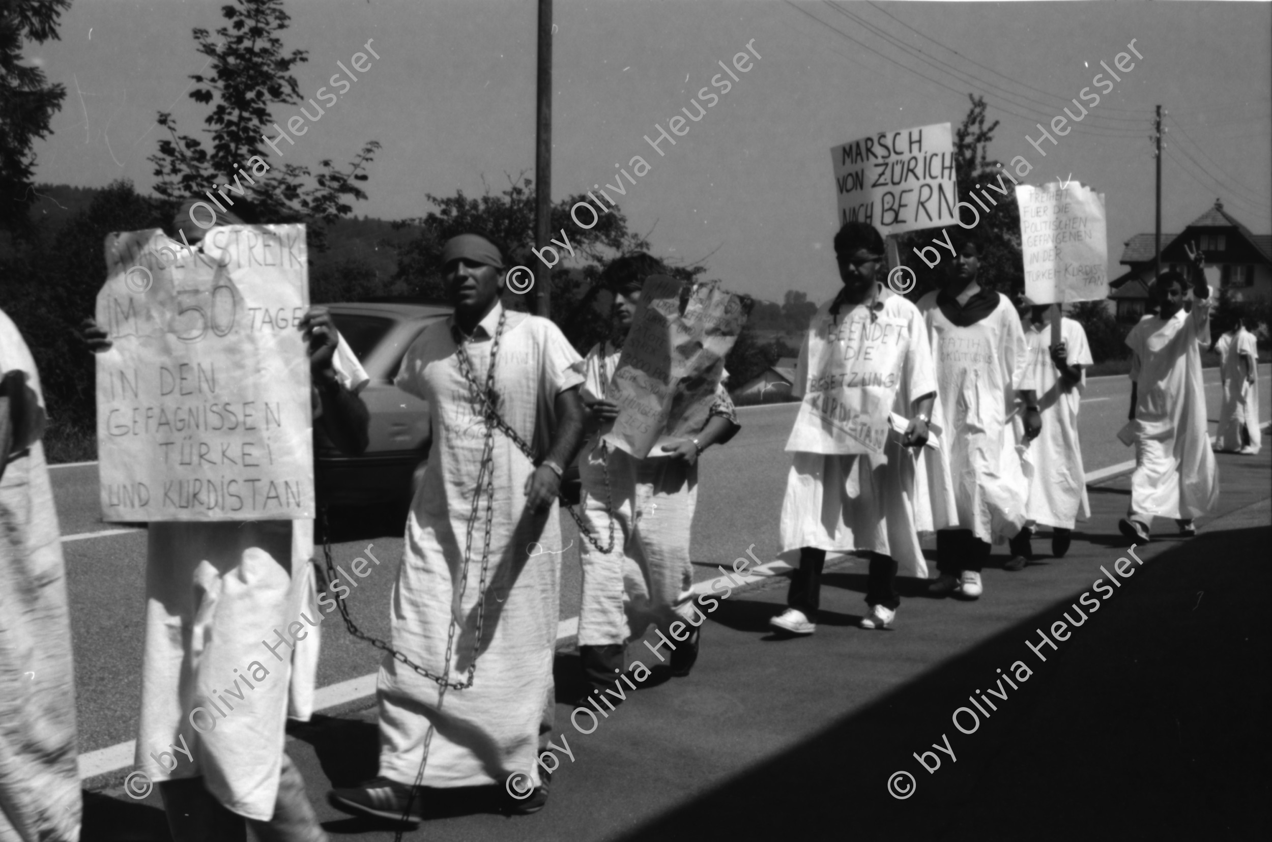 Image of sheet 19890700 photo 21: 20 Kurden gehen in einem Protestmarsch von Zürich nach Bern zu Fuss. Protest gegen die Ausschaffungspolitik der Schweizer Regierungen. Die ländliche Bevölkerung hat kein Interesse an der Informationen der Kurden. Sie warten auf ein Radfahrer Velorennen rennen. In einer Badeanstalt. Dicker fetter Mann mit glanz auf der Brust in Badehose im Schwimmbad. Bäbe Weber und Pierre Mennel tanzen auf dem 'Felde'.