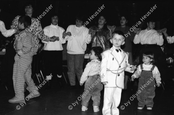 Image of sheet 19890860 photo 19: Demonstration im Kasernen Innenhof. Modepuppe sitzt an Nähmaschine im Freien. In einem Lebensmittelladen für TürkInnen. Asyl bewerber Innen. Uniformen hängen da, während Männer essen. Zwei Frauen stehen da. Unbekannte Gestalt beim Telefonieren in Telefon Kabine. Schliessung eines Ladens. Zwei Männer als Türkisches Beschneidung fest in einer Turnhalle in Pratteln. Frauen und Kinder und Männer tanzen zusmmen . Basel Brauchtum turkish boy circumcision child tradition muslim religion asylum seekers human rights Switzerland Schweiz 1989