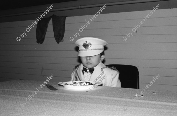 Image of sheet 19890860 photo 21: Demonstration im Kasernen Innenhof. Modepuppe sitzt an Nähmaschine im Freien. In einem Lebensmittelladen für TürkInnen. Asyl bewerber Innen. Uniformen hängen da, während Männer essen. Zwei Frauen stehen da. Unbekannte Gestalt beim Telefonieren in Telefon Kabine. Schliessung eines Ladens. Zwei Männer als Türkisches Beschneidung fest in einer Turnhalle in Pratteln. Frauen und Kinder und Männer tanzen zusmmen . Basel Brauchtum turkish boy circumcision child tradition muslim religion asylum seekers human rights Switzerland Schweiz 1989