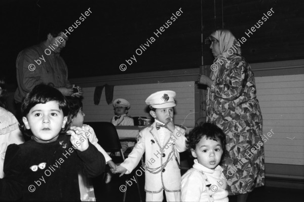 Image of sheet 19890860 photo 28: Demonstration im Kasernen Innenhof. Modepuppe sitzt an Nähmaschine im Freien. In einem Lebensmittelladen für TürkInnen. Asyl bewerber Innen. Uniformen hängen da, während Männer essen. Zwei Frauen stehen da. Unbekannte Gestalt beim Telefonieren in Telefon Kabine. Schliessung eines Ladens. Zwei Männer als Türkisches Beschneidung fest in einer Turnhalle in Pratteln. Frauen und Kinder und Männer tanzen zusmmen . Basel Brauchtum turkish boy circumcision child tradition muslim religion asylum seekers human rights Switzerland Schweiz 1989