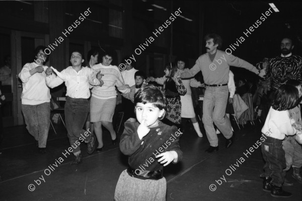 Image of sheet 19890860 photo 31: Demonstration im Kasernen Innenhof. Modepuppe sitzt an Nähmaschine im Freien. In einem Lebensmittelladen für TürkInnen. Asyl bewerber Innen. Uniformen hängen da, während Männer essen. Zwei Frauen stehen da. Unbekannte Gestalt beim Telefonieren in Telefon Kabine. Schliessung eines Ladens. Zwei Männer als Türkisches Beschneidung fest in einer Turnhalle in Pratteln. Frauen und Kinder und Männer tanzen zusmmen . Basel Brauchtum turkish boy circumcision child tradition muslim religion asylum seekers human rights Switzerland Schweiz 1989