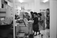 Image of sheet 19890860 photo 7: Demonstration im Kasernen Innenhof. Modepuppe sitzt an Nähmaschine im Freien. In einem Lebensmittelladen für TürkInnen. Asyl bewerber Innen. Uniformen hängen da, während Männer essen. Zwei Frauen stehen da. Unbekannte Gestalt beim Telefonieren in Telefon Kabine. Schliessung eines Ladens. Zwei Männer als Türkisches Beschneidung fest in einer Turnhalle in Pratteln. Frauen und Kinder und Männer tanzen zusmmen . Basel Brauchtum turkish boy circumcision child tradition muslim religion asylum seekers human rights Switzerland Schweiz 1989
