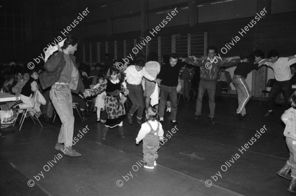 Image of sheet 19890870 photo 0: frtsg. 890860 Türkisches Beschneidungs ritual fest in einer Turnhalle in Pratteln. Frauen und Männer und Kinder tanzen. Ein Mädchen führt die Gruppe mit einem weissen Taschentuch. Zwei alte Männer sitzen neben dem kleinen Jungen in Uniform. Bild mit seiner Familie. Priska Fetz von Aarau tanzt auch mit. Familiengruppenbild. Kanton Baselland 1989  Schweiz Turkey Türkei Refugees Flüchtlinge Boy circumcision