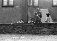 Image of sheet 19900110 photo 15: Portrait vor Ofen im Erismannhof. Städtische Siedlung Zürich 
Iris Zoe und Ruedi Teklenburg. Carla Lia Monti 'Räuberinnen' Ofen Erismannhof 2. Kindergarten. Kinder spielen mit Gewehren. Achmed von Warthburg. Fahrrad in der Stube. X liegt auf Sofa. Carla Lia Monti beim Haareschneiden. Sadam Hussein auf Poster. Zürich 1990