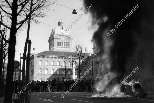 Image of sheet 19900150 photo 6: A masked protester in front of a burning car in front of the Parliament Building of the Bundeshaus.

Der sogenannte Fichenskandal (auch Fichenaffäre) ist ein Skandal der neueren Schweizer Geschichte in der Endphase des Kalten Krieges. Fiche [ˈfiʃə] ist die französische Bezeichnung für Karteikarte. Davon abgeleitet hat sich in der Schweiz das Wort «Fichenstaat» als Umschreibung für einen «Schnüffelstaat» gebildet

The Fichenaffäre or Secret Files Scandal shook public opinion in Switzerland in 1989. That year, it was revealed that the Swiss federal authorities, as well as the cantonal police forces, had put in place a system of mass surveillance of the population