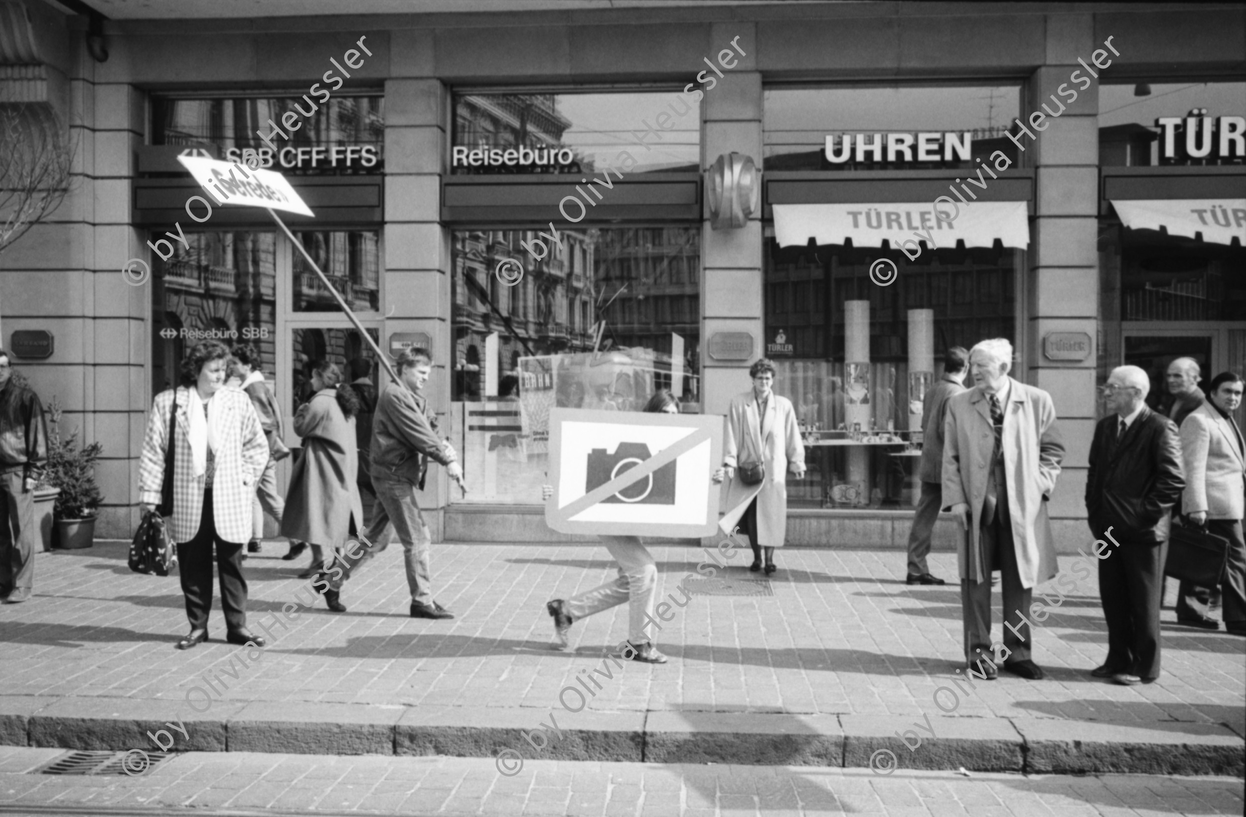 Image of sheet 19900170 photo 28: Am Paradeplatz startet die Aktion »Fotografieren verboten«, Zürich 1990. 
Tafel «Gerede» . Emil Sonderegger Oberstdivisionär Kommandant der Ordunungstruppen in Zürich.
leitete 1916 Aktion gegen Arbeiter in Zürich. Stefan Nestler. Kind. VBZ Kasten alter. Tafel mit Mona Lisa als Mona Sonderegger. Aleks Weber (gest.) Aktion übernommen von Kurt Buchwald, Photograph Berlin. Zwei Küssende und Tafel. Sabine Zürich