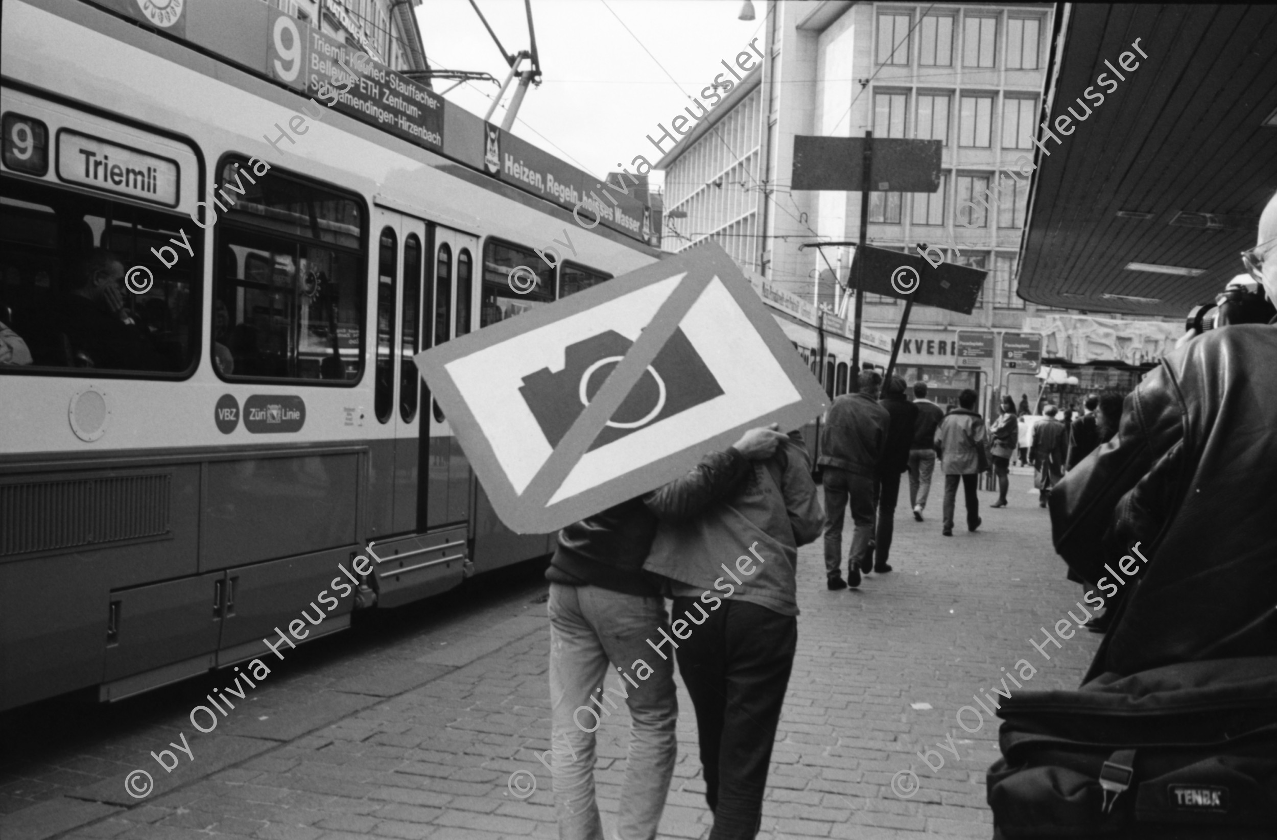 Image of sheet 19900170 photo 33: Am Paradeplatz startet die Aktion »Fotografieren verboten«, Zürich 1990. 
Tafel «Gerede» . Emil Sonderegger Oberstdivisionär Kommandant der Ordunungstruppen in Zürich.
leitete 1916 Aktion gegen Arbeiter in Zürich. Stefan Nestler. Kind. VBZ Kasten alter. Tafel mit Mona Lisa als Mona Sonderegger. Aleks Weber (gest.) Aktion übernommen von Kurt Buchwald, Photograph Berlin. Zwei Küssende und Tafel. Sabine Zürich
