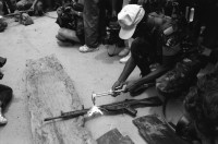 Image of sheet 19900310 photo 24: UN-Helikopter landet unter Aufsicht eines UN Soldaten auf kleinem Hügel in Yamales. Alte ausgediente unbrauchbare Waffen liegen zum symbolischen Zerstörungsakt der UN Truppen auf einer Plane bereit. Junge posiert dazwischen. Portrait Nr. 8 Beretta und Nr. 7 Uzi Italienische und israelische Klein maschinen gewehre. Staub. 12 General Quesada. 13 und 14 Cmdte. Siro Somozist. UN-Soldaten brennen die Waffen nieder. Kriegs Zerstörung mit Flammenwerfer. UN Soldaten sind mit Deutschen Heckler und Koch bewaffnet. Honduras Yamales 1990 rifle weapon arms