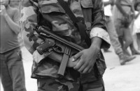 Image of sheet 19900310 photo 8: UN-Helikopter landet unter Aufsicht eines UN Soldaten auf kleinem Hügel in Yamales. Alte ausgediente unbrauchbare Waffen liegen zum symbolischen Zerstörungsakt der UN Truppen auf einer Plane bereit. Junge posiert dazwischen. Portrait Nr. 8 Beretta und Nr. 7 Uzi Italienische und israelische Klein maschinen gewehre. Staub. 12 General Quesada. 13 und 14 Cmdte. Siro Somozist. UN-Soldaten brennen die Waffen nieder. Kriegs Zerstörung mit Flammenwerfer. UN Soldaten sind mit Deutschen Heckler und Koch bewaffnet. Honduras Yamales 1990 rifle weapon arms