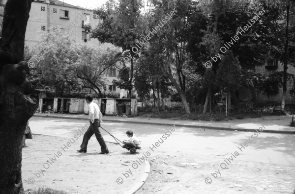 Image of sheet 19900410 photo 18: Kinder spielen mit 'Gondel' in Wohnsiedlung. Soldaten, Mütter und Väter etc.  legen auf einem neuen Friedhof für ihre gefallenen Freunde u/o Brüder und Söhne Blumen nieder. Wachsresten. Flugzeug Propeller Flügel. Portrait Susan und Judith (ihre Tochter) Hotel in Sibiu gebaut von Sohn Cheaucescu's. Edel Restaurant. Kind malt auf Strasse mit Kreide. Vater und Kind (im selbstgebastelten Kinderwagen). Markt. Rumania Romania 1990