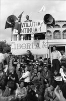 Image of sheet 19900510 photo 12: Ich gehe mit Tomo Muscionico durch die Strassen und fotografiere ihn wie er ein kleines Mädchen vor einer Plakatwand (und zerschossenem Haus) ablichtet. Im Hotel schläft auch Nachtway auf einem Stuhl und er wird gefilmt! Kult. Auf dem Universitätsplatz Demonstration Protest 'Revolutia Continua' Menschen stehen vor Lautsprecher und Transparent Hotel Bucuresti. Grossvater Mihai und Blanca im Schoss ihrer Urgrossmutter. In Sibiu ist die erste öffentliche Orthodoxen Zelebrierung auf der Strasse. Rumänien Romania Rumania 1990

The Roma (Roma in Romani; Romi or Țigani in Romanian) constitute one of the largest minorities in Romania. According to the 2011 census, they number 619,007 people or 3.2% of the total population, being the second-largest ethnic minority in Romania after Hungarians. The Roma are Romania's most socially and economically disadvantaged minority, with high illiteracy levels