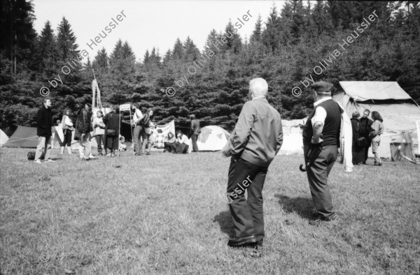 Image of sheet 19900540 photo 12: Das Waffenplatzgegner Camp steht kurz vor der polizeilichen Räumung. Zwischen den Zelten stehen zwei Holz plastiken. Auf einem Plakat küssen sich zwei Polizei Grenadiere Endart. zwei Bauern besuchen das Camp. Portrait Ein Theologe Pfarrer Jonas zeichnet. Der Zaun um den Waffenplatz. Securitas. Protectas. ? Die Grenadiere räumen. 1990 Neuchlen Anschwilen St. Gallen Waffenplatz Gewaltfreie Aktion Militär military army armee protest