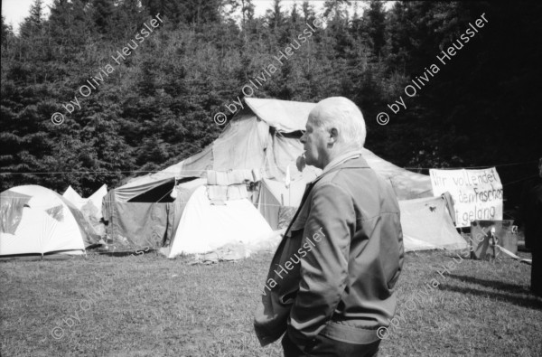 Image of sheet 19900540 photo 15: Das Waffenplatzgegner Camp steht kurz vor der polizeilichen Räumung. Zwischen den Zelten stehen zwei Holz plastiken. Auf einem Plakat küssen sich zwei Polizei Grenadiere Endart. zwei Bauern besuchen das Camp. Portrait Ein Theologe Pfarrer Jonas zeichnet. Der Zaun um den Waffenplatz. Securitas. Protectas. ? Die Grenadiere räumen. 1990 Neuchlen Anschwilen St. Gallen Waffenplatz Gewaltfreie Aktion Militär military army armee protest